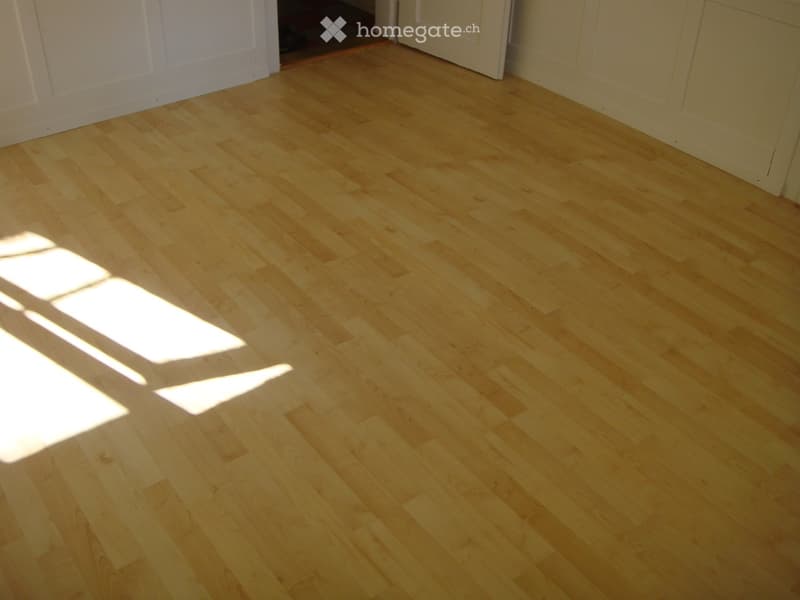 Empty room with light wooden flooring and white walls, featuring a doorway leading to another space.