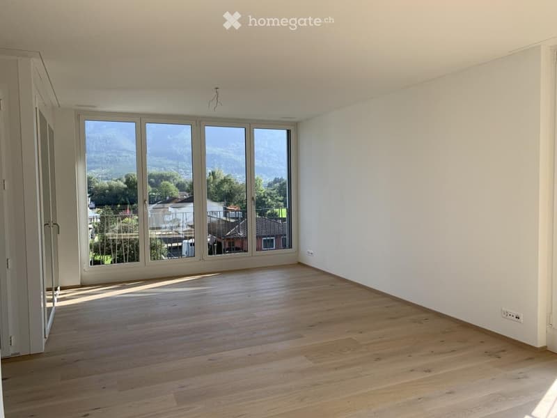 Empty room with wooden flooring, large windows offering a scenic mountain view, and white walls.