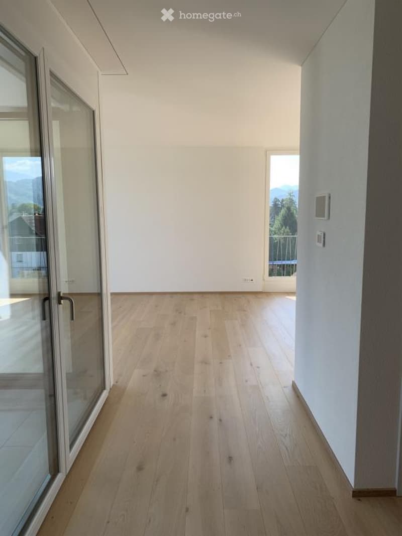 Empty room with light wooden flooring, large glass doors leading to a balcony with a scenic mountain view.