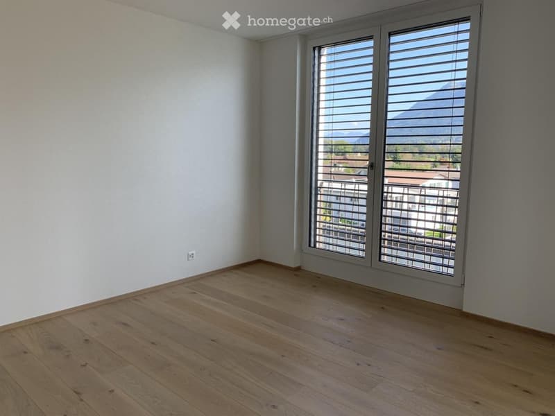 Empty room with wooden flooring, white walls, large window with blinds, and a scenic mountain view outside.