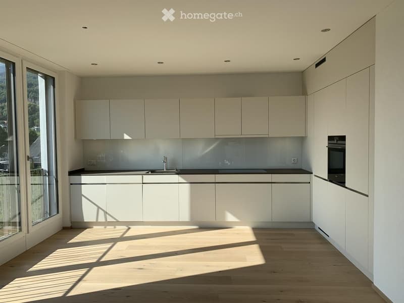Modern kitchen with white cabinets, a black countertop, and a large window offering a scenic view. The space features a sleek sink, a faucet, and an oven, all illuminated by natural light.
