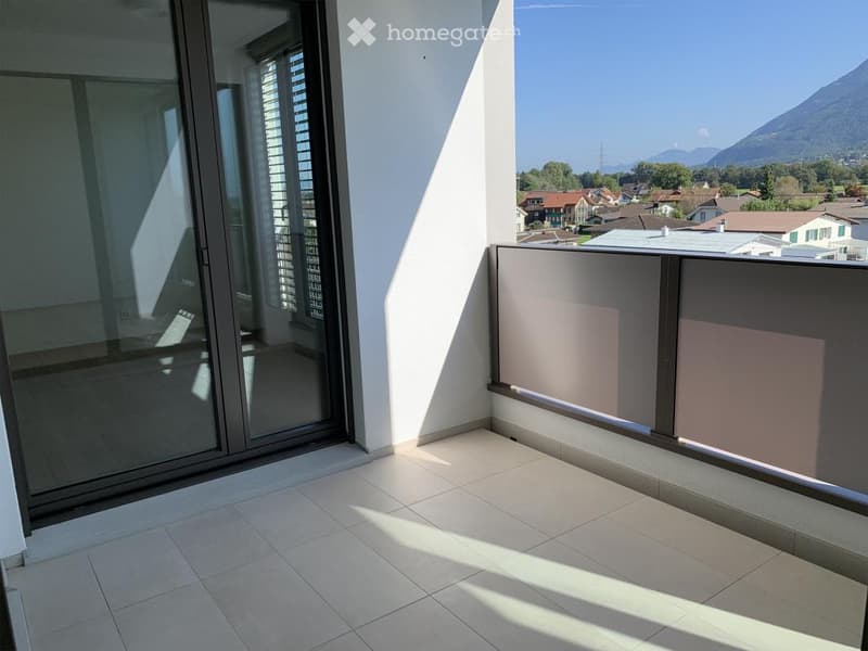 Modern balcony with tiled floor, large glass sliding doors, and a scenic mountain view in the background.