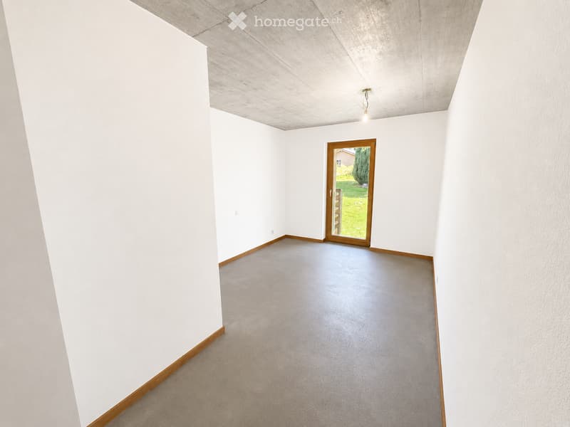 Empty room with white walls, grey carpeted floor, and a wooden-framed sliding door leading to a green outdoor area.