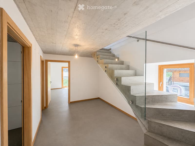 Modern hallway with a concrete staircase, glass railing, wooden doors, and exposed wooden ceiling beams.