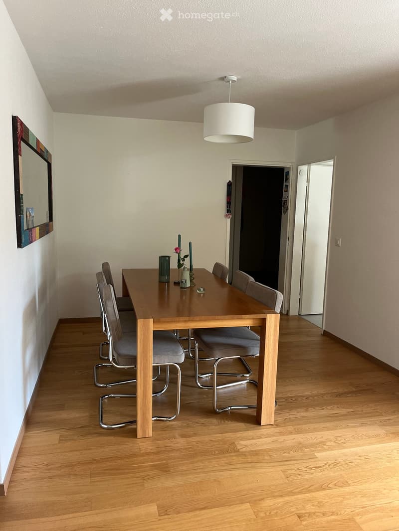 Dining room with wooden floor, dining table, six chairs, vase with flower, candles, and a mirror on the wall.