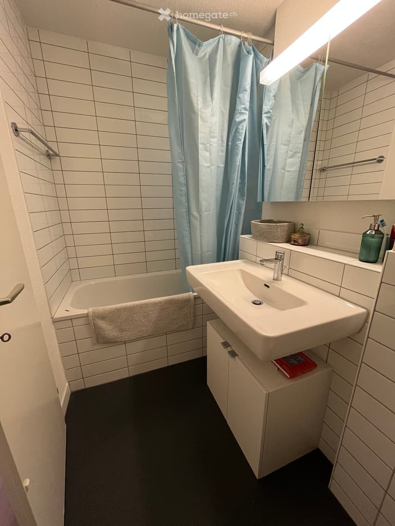 Modern bathroom with white tiled walls, a bathtub, a sink with a mirror, and a towel on the edge of the tub.