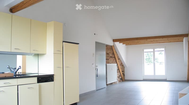 Bright kitchen with light yellow cabinets, a sink, a dishwasher, and a tiled floor. Exposed wooden beams on the ceiling and a brick accent wall are visible.