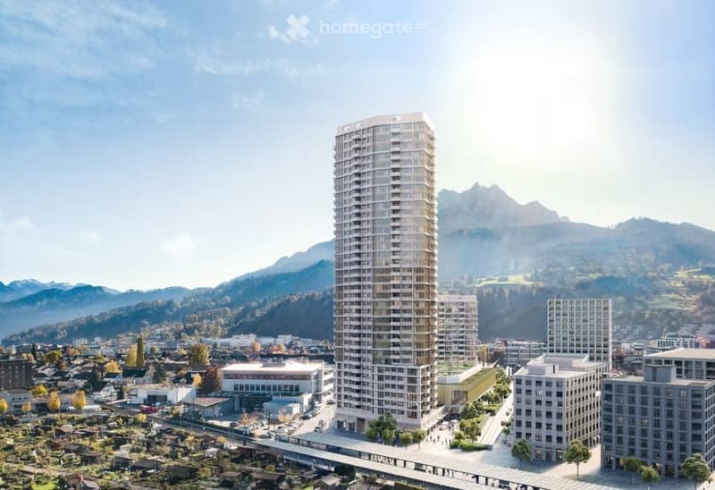 A modern high-rise building surrounded by smaller structures and a scenic mountainous backdrop.