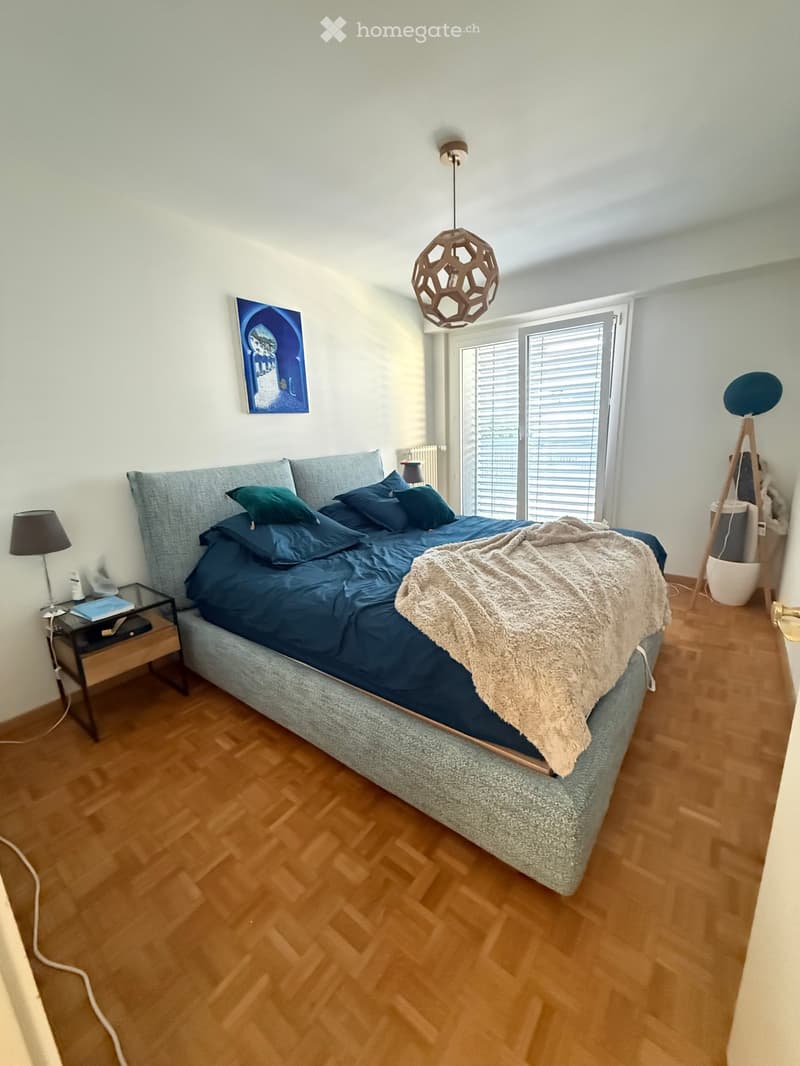 Modern bedroom with a large bed, nightstand, pendant light, and artwork on the wall.