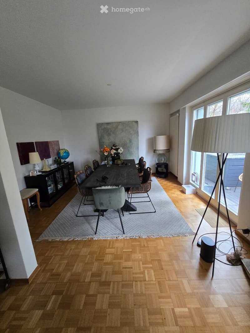 large dining area, hardwood floors, windows with curtains, a long table with chairs, various lamps, rug, wooden cabinet, artwork on the wall
