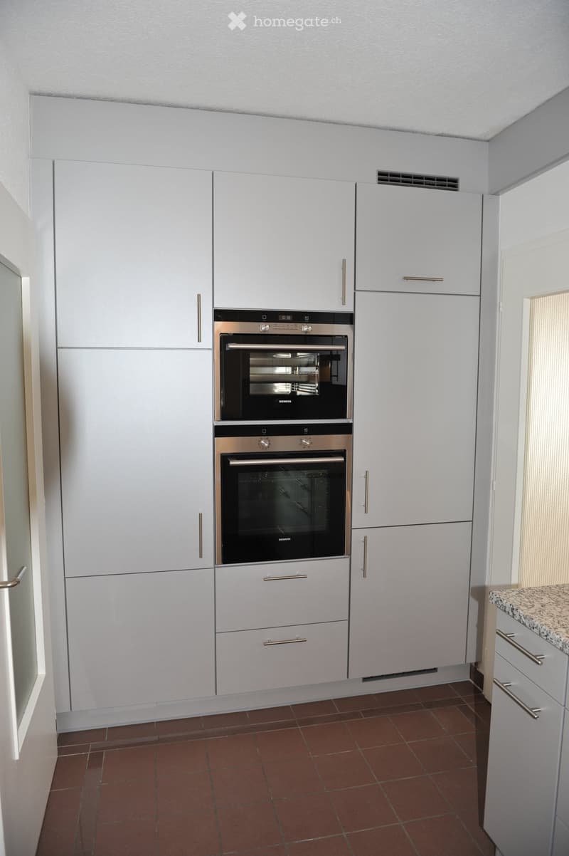 White cabinets, stainless steel handles, brown tiled floor, double oven, dishwasher, modern lighting