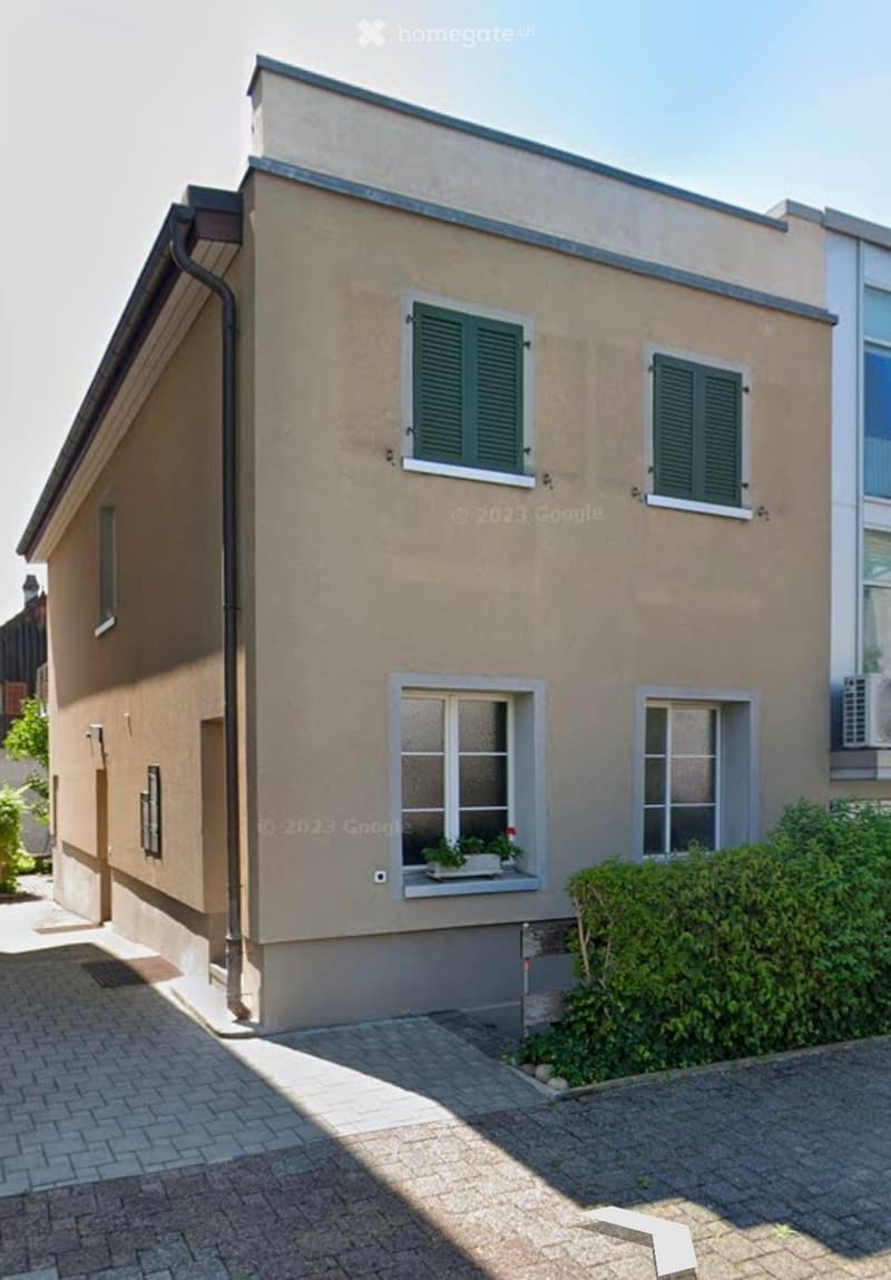 Two-story house with beige exterior, green shutters, and a small window planter with flowers.