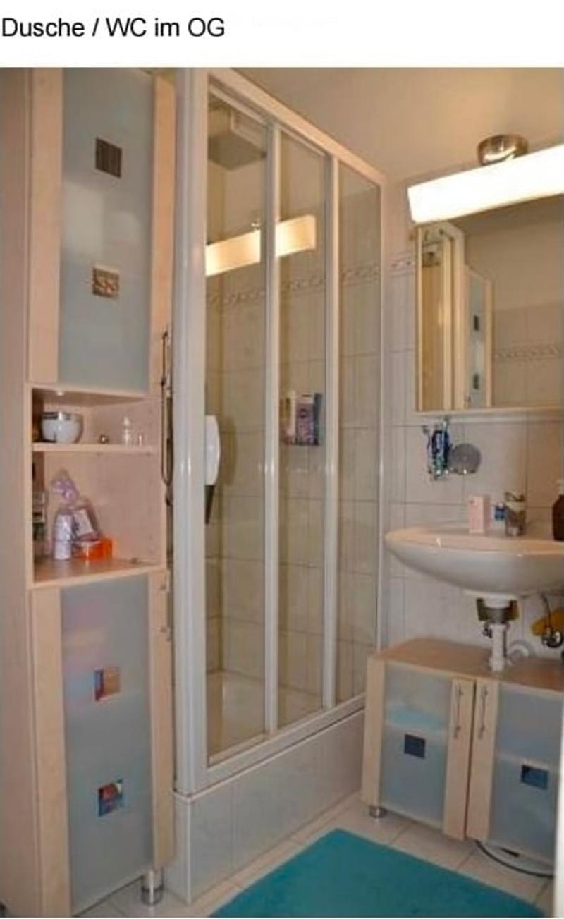 Bathroom with a glass-enclosed shower stall, a sink with a mirror above it, and a small cabinet with shelves for storage.