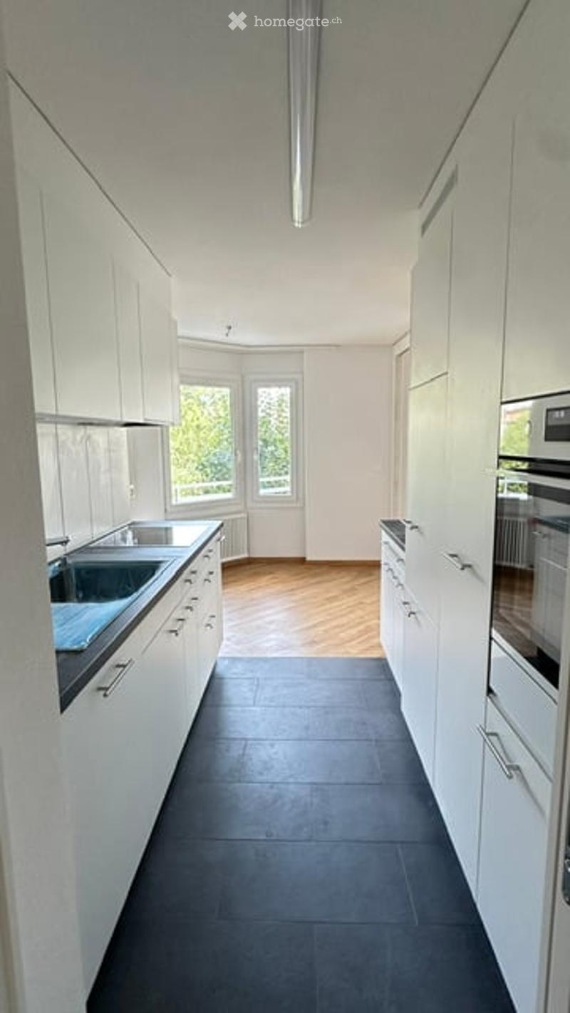 Modern kitchen with white cabinets, dark tiled floor, and stainless steel sink.