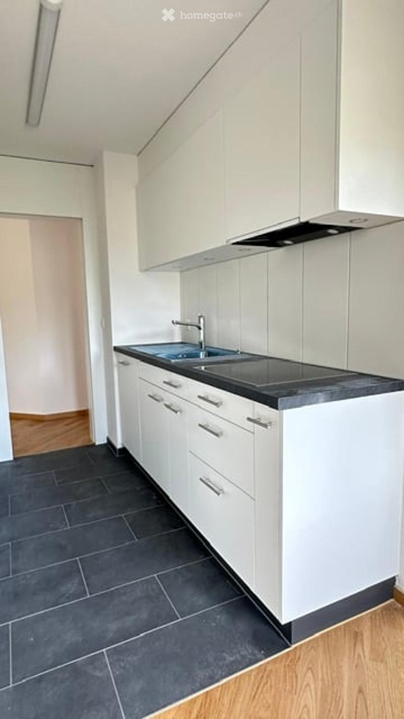 Modern kitchen with white cabinets, black countertops, and dark tiled flooring. Features a sink with a modern faucet and built-in storage drawers.