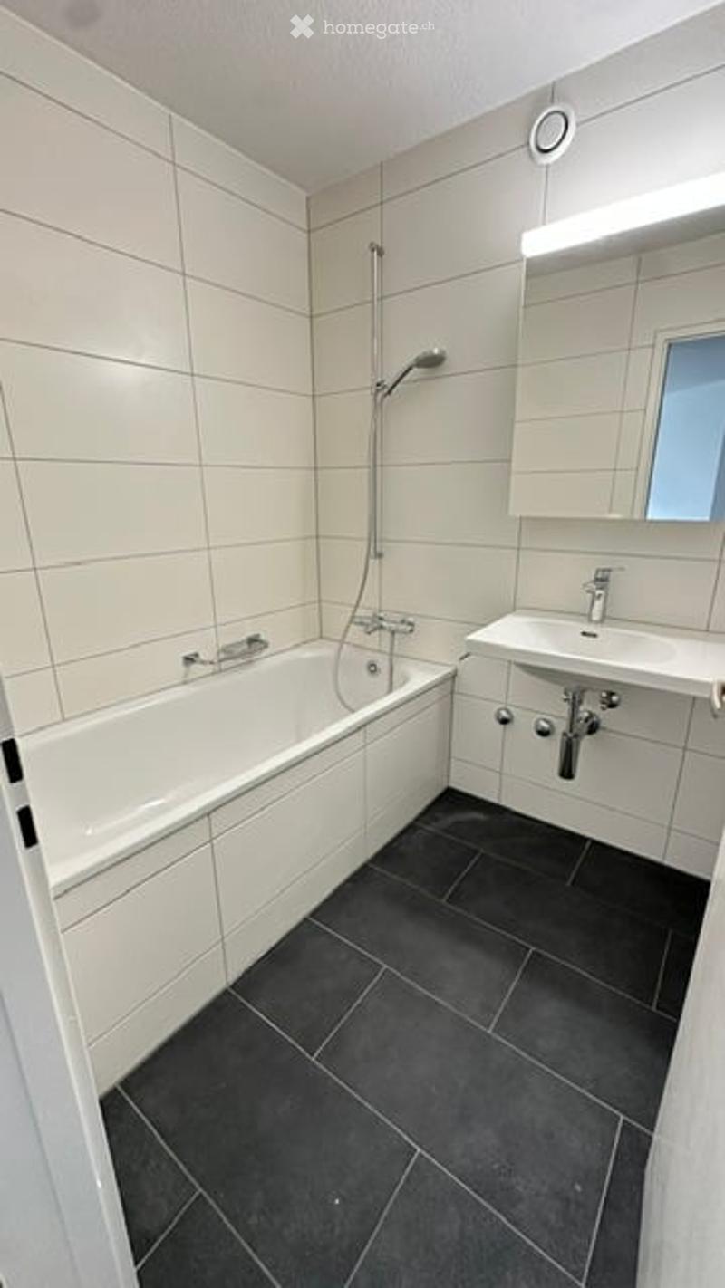 Modern bathroom with white tiles, a bathtub, a sink, and a mirror above it.