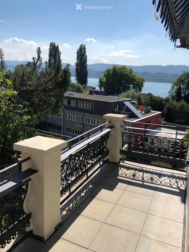 Balcony with ornate metal railing, overlooking a scenic lake and distant mountains.