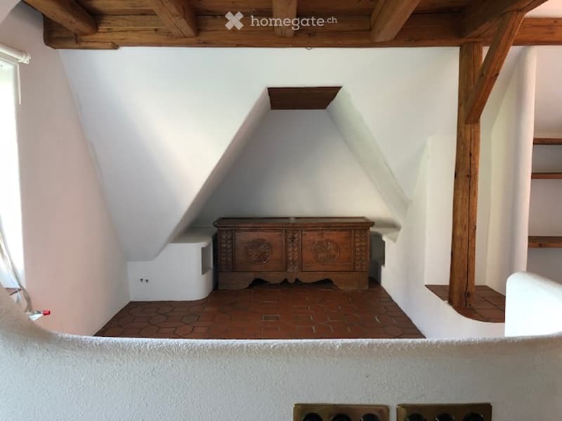 Attic room with exposed wooden beams, slanted ceilings, brick floor, and a wooden chest.