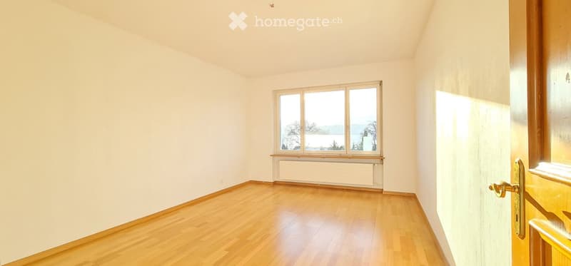 Empty room with wooden flooring, white walls, and a large window offering a view of the outdoors.