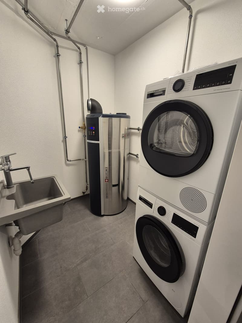 Modern bathroom with a washing machine, dryer, sink, and water heater. The space features tiled flooring and white walls.
