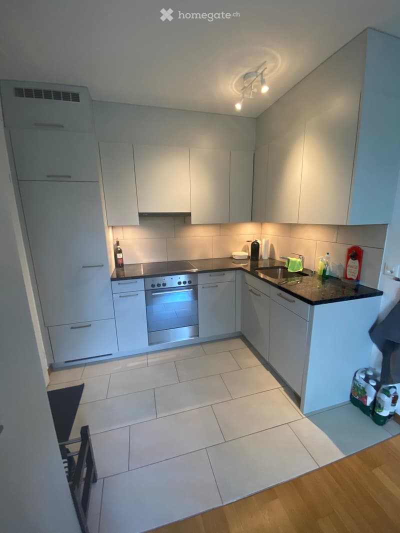Modern kitchen with white cabinets, stainless steel oven, sink, and countertop items including a bottle, cup, and water bottles.