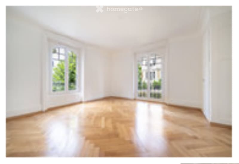 Empty room with wooden flooring and white walls, featuring two large windows with white frames.