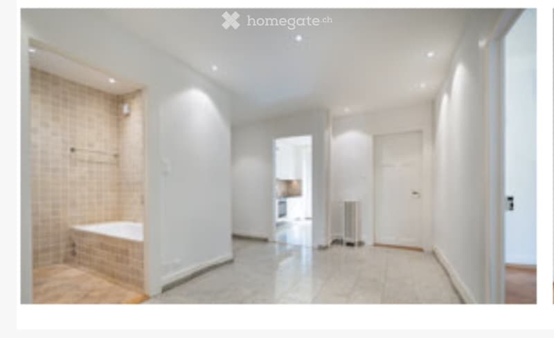 Bright hallway with white walls, tiled floor, and a visible bathroom with a bathtub and shower area.