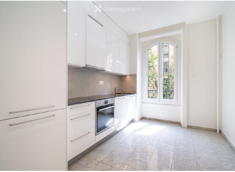 Modern kitchen with white cabinets, stainless steel oven, sink, and faucet, large window with view of greenery.