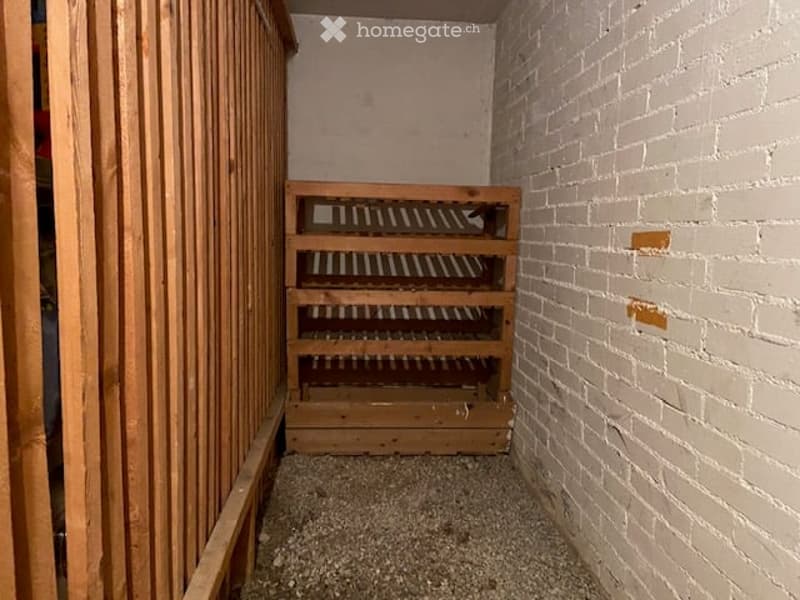 Empty storage room with exposed brick walls, wooden shelving unit, and gravel floor.