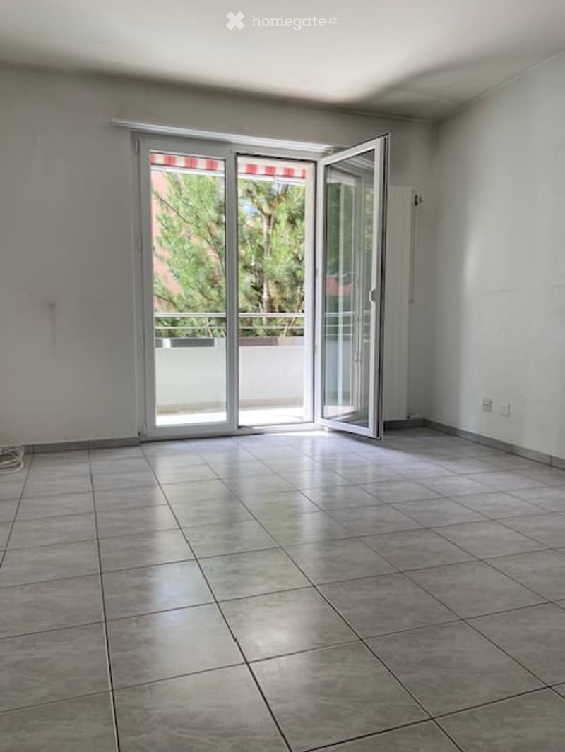 Empty room with tiled floor, large sliding glass doors leading to a balcony, white walls, and a radiator on the right side.