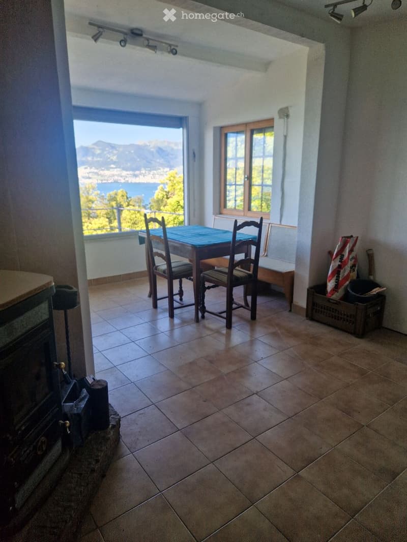 Bright room with tiled floor, fireplace, table with chairs, bench, and scenic mountain view through large windows.