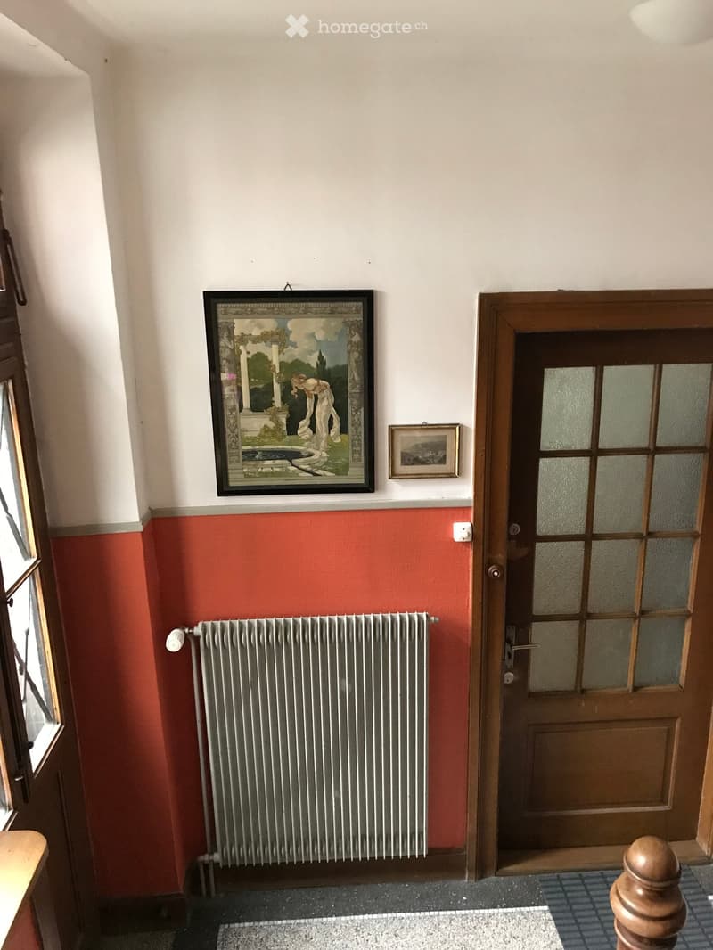Hallway with red lower walls, white upper walls, a radiator, framed artwork, and a wooden door with glass panels.