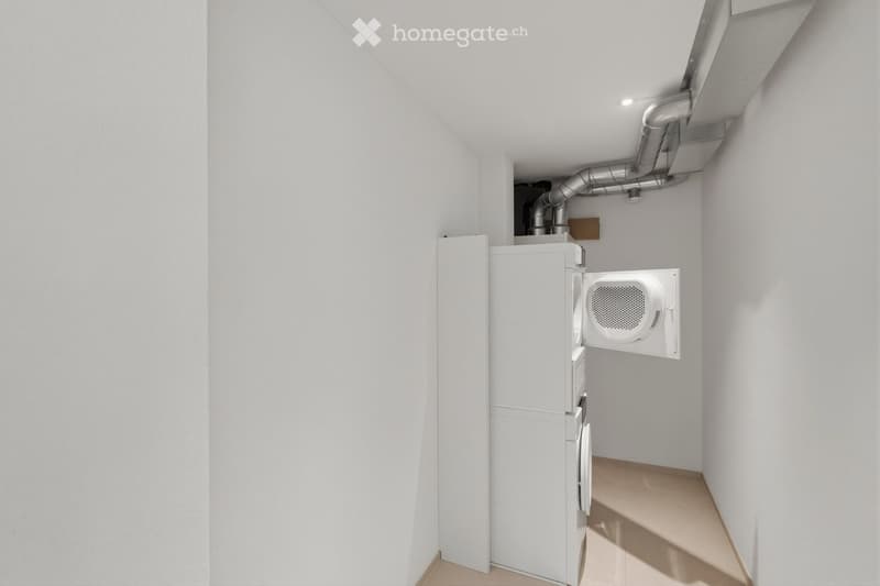 A small, clean utility room with white walls and a light-colored floor. It contains a white washing machine and a white dryer, both positioned against the wall.