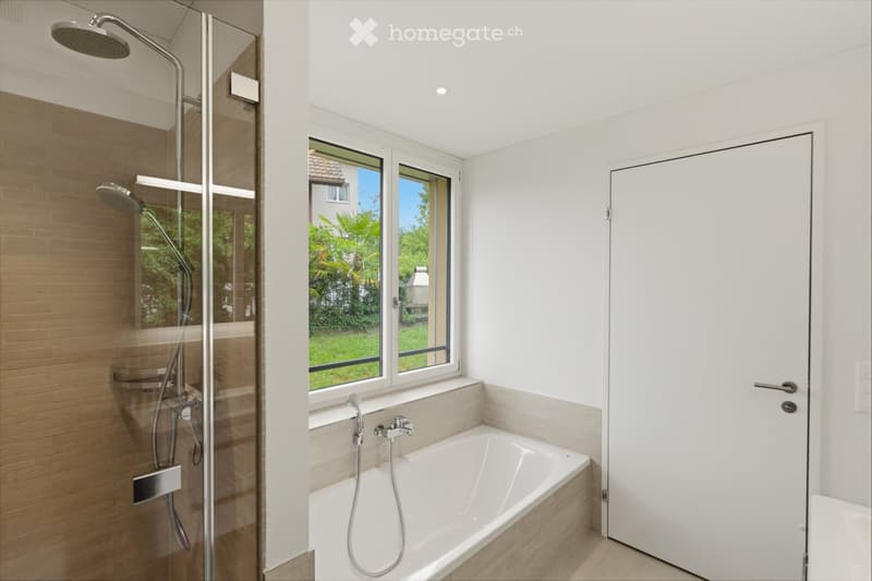 Modern bathroom with a bathtub, separate shower area, and large windows offering a view of the garden.