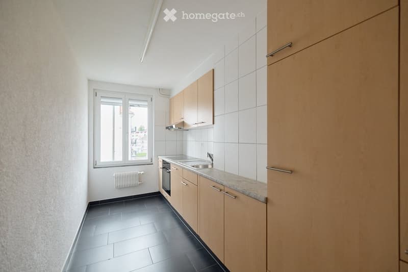 Modern kitchen with light wooden cabinets, granite countertop, stainless steel sink and faucet, black tiled floor, and a window with a view.