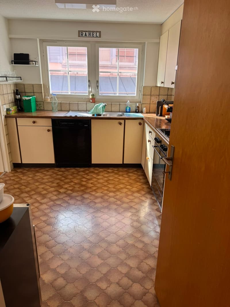 Kitchen with light-colored cabinets, a dishwasher, oven, and countertop. The floor has a patterned tile design.