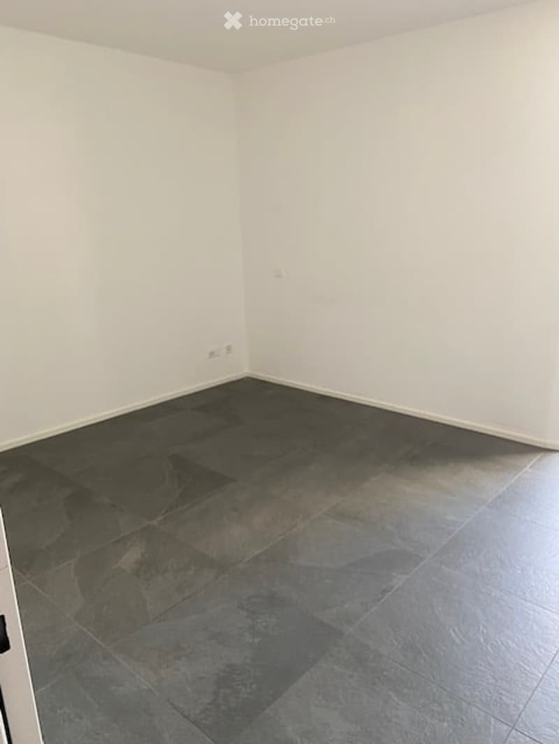 Completely empty room with white walls and dark grey tiled floor. No furniture or equipment.