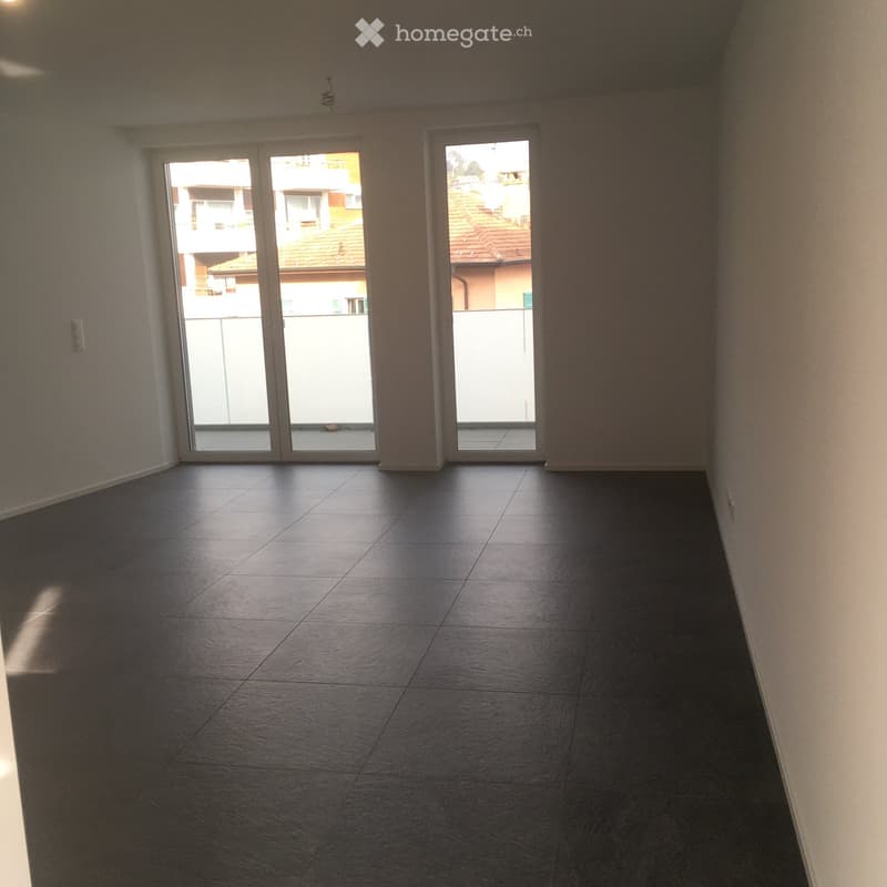 Empty room with dark tiled flooring and large sliding glass doors leading to a balcony area.