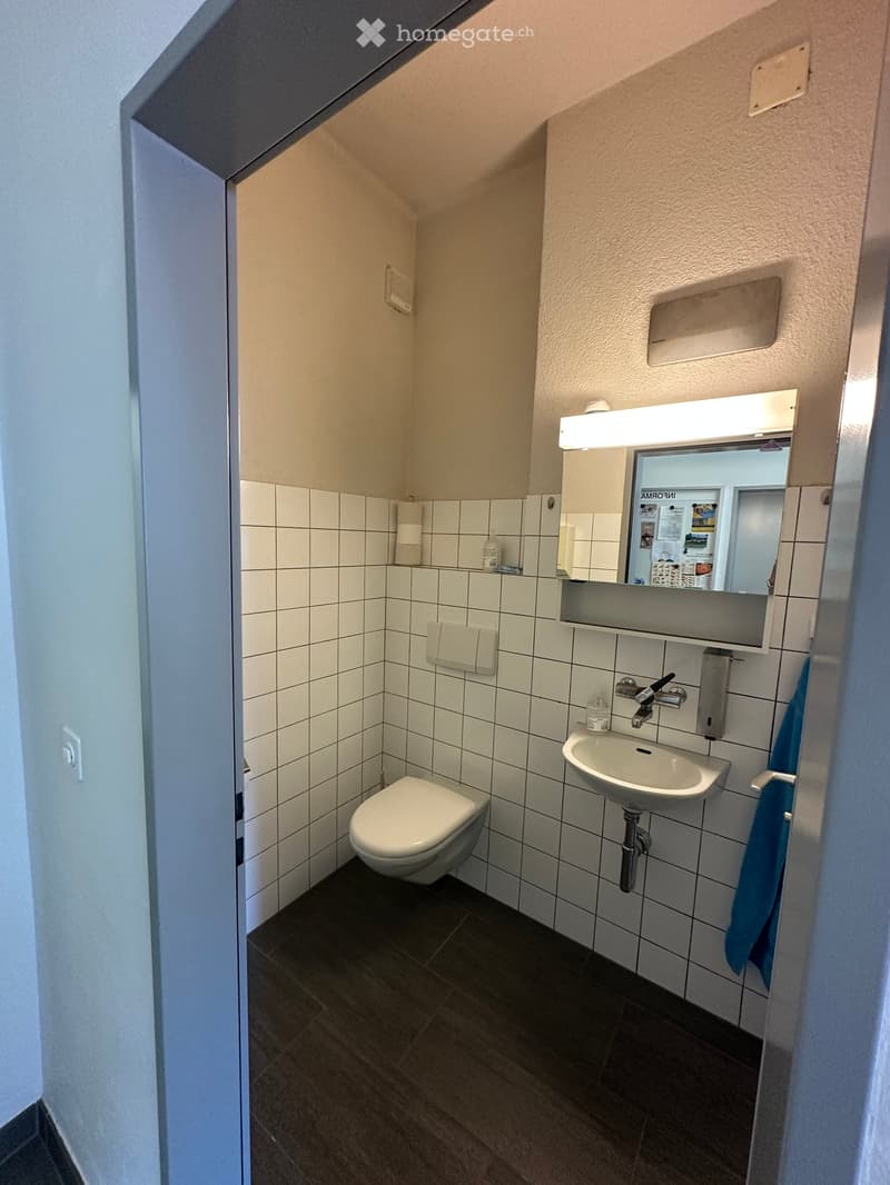 Compact bathroom with white tiled walls, a toilet, a sink with a mirror, and a towel hanging on the side.