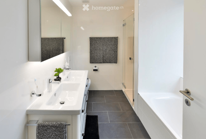 Modern bathroom with a double sink, mirror, toilet, bathtub, and decorative towels. Features a sleek design with a potted plant on the sink counter.
