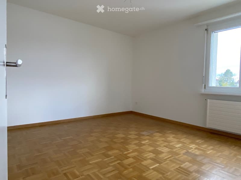 Empty room with light-colored walls, wooden flooring, and a single window with white frame and radiator below it.