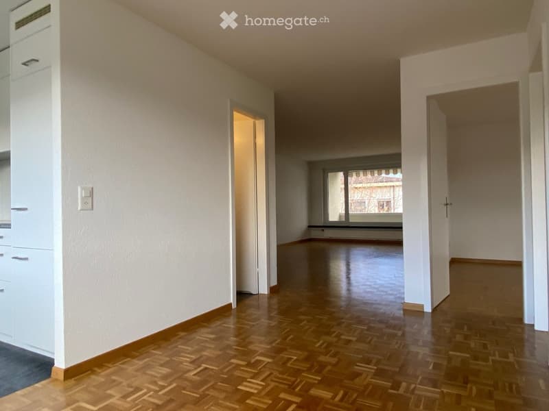 Empty hallway with wooden flooring, white walls, and a large window at the end.
