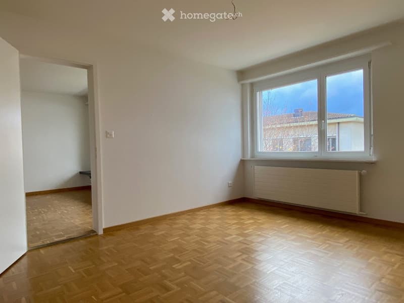 Empty room with wooden flooring, white walls, and a large window with a radiator below it.
