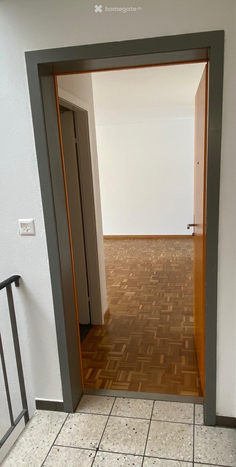 Open doorway leading to a hallway with wooden flooring and white walls.