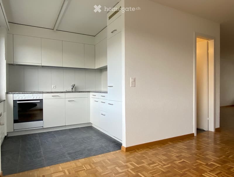 Modern kitchen with white cabinets, stainless steel oven, and grey tiled floor. Wooden flooring extends into adjacent space.