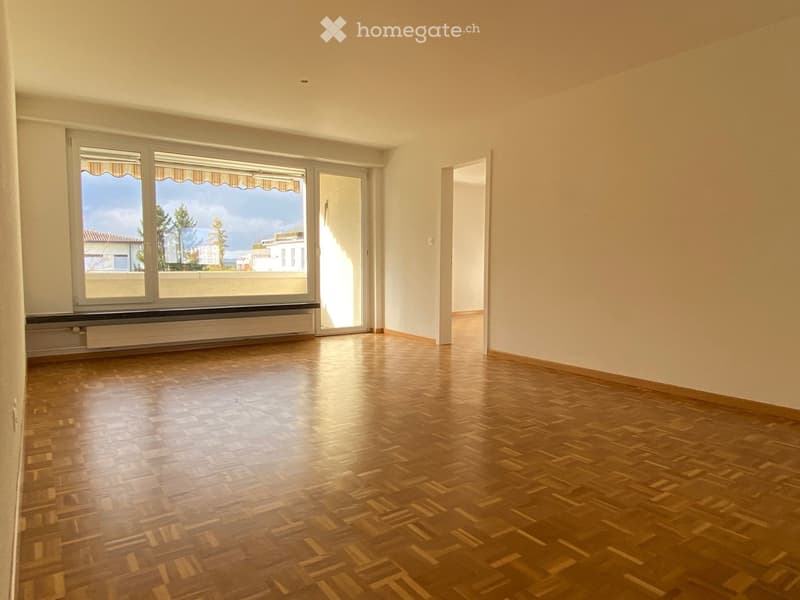 Empty room with wooden flooring, large windows with blinds, and a view of the outside area.