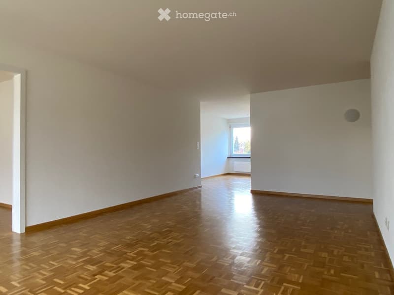 Empty hallway with wooden flooring and white walls, featuring a window at the end.