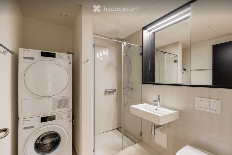 Modern bathroom with a washing machine, shower, sink, and mirror.
