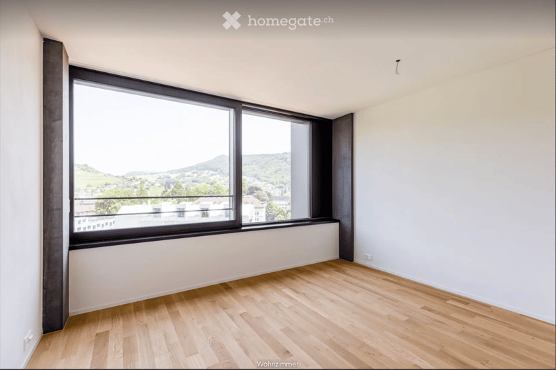 Empty room with light wooden flooring, white walls, and large windows offering a scenic view of the landscape.