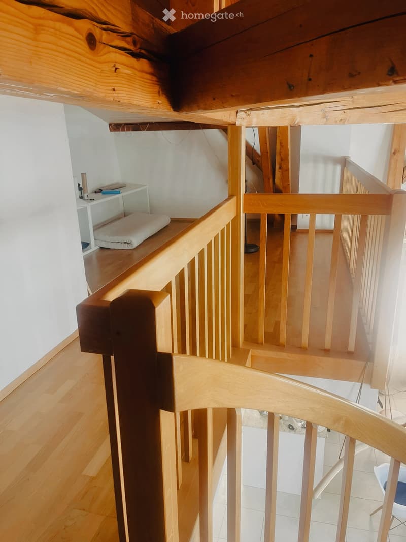 Wooden staircase with a handrail and a small shelf on the landing, leading to a lower level with tiled flooring.